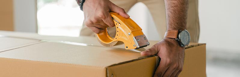 Person sealing a moving box with tape.