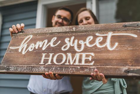 Couple holding a ‘home sweet home’ sign.