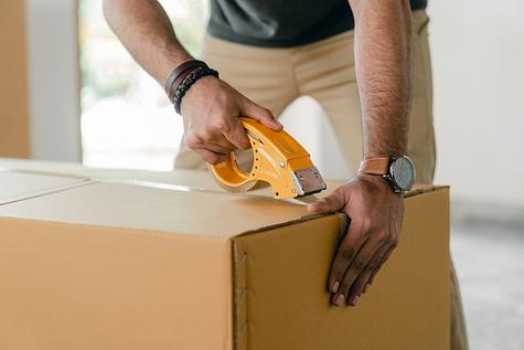Person sealing a moving box with tape.