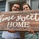 Couple holding a ‘home sweet home’ sign.