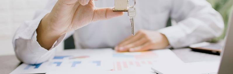 Person holding a house key with charts on the table.
